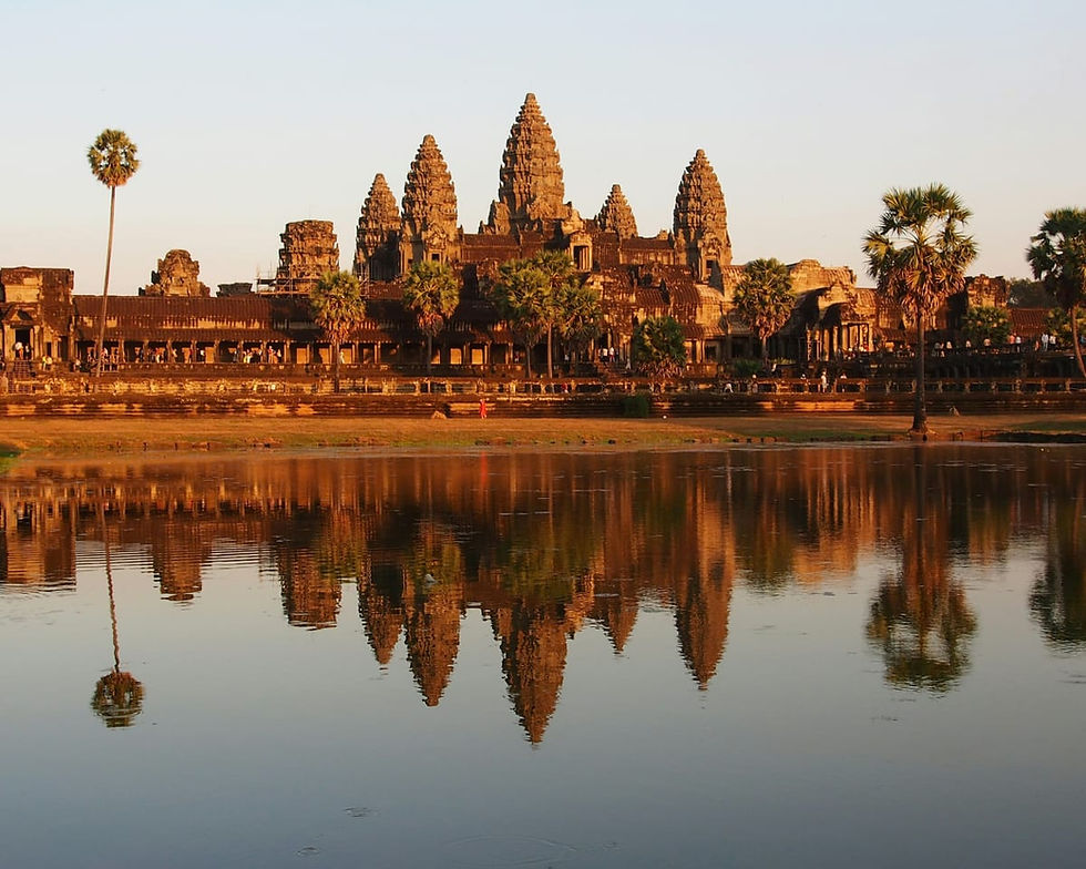 The iconic stone towers of Angkor Wat in Cambodia reflected in a still pond at golden hour.