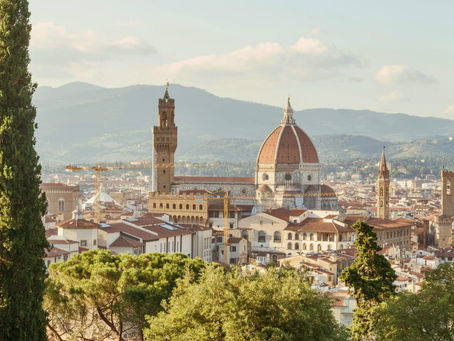 Panoramic skyline view of Florence featuring Brunelleschi's Dome and Palazzo Vecchio framed by green cypress trees.