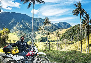 Suzuki DR650 on a gravel road framed by wax palms and green Andean slopes.