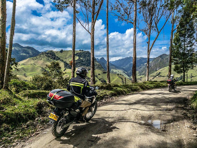 Motorcycle riding on a dirt road through eucalyptus trees with green Colombian Andean hills and mountains in the background.