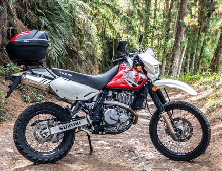 Side profile of a Suzuki DR650 dual-sport on compact dirt with protective hardware installed.