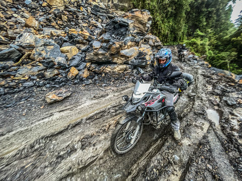 Motorcyclist riding through muddy off-road mountain trail in Colombia Coffee Region Andes.