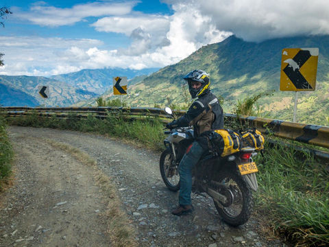 Adventure motorcyclist riding dirt switchback road in Colombian Andes Coffee Region.