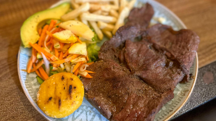 Plate of grilled steak served with arepa, avocado, salad, and fries in Colombia.