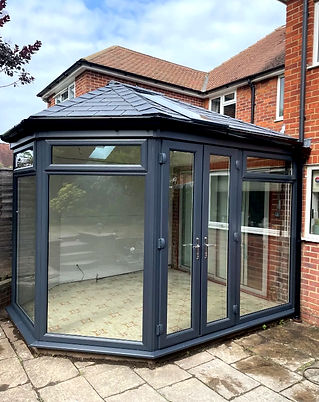 Glass conservatory with dark grey frame attached to a brick house