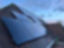 A side-angle view looking upward at dark solar panels covering a slate tile roof