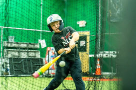 Young baseball player hitting a ball in a batting cage