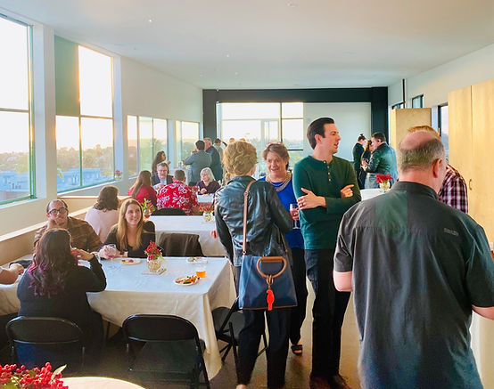 A group of people gathered in a dining area with large windows and white tables.