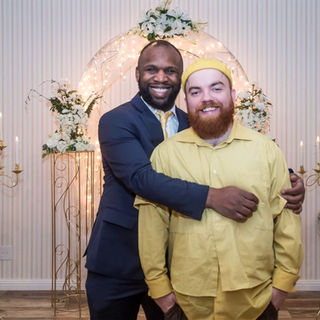 Happy grooms embracing at their wedding under a beautiful floral arch.