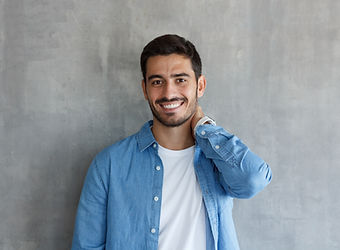 Smiling man in blue shirt and white tee, Regular Haircut, gray wall background.