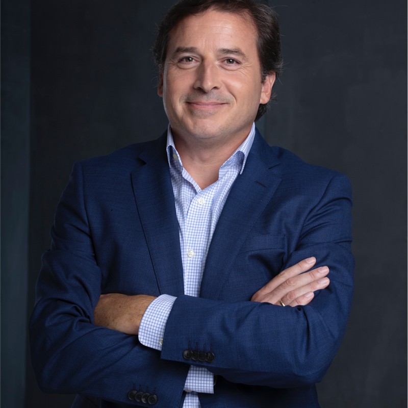 Smiling man wearing a blue suit with a blue button down shirt, with his arms crossed
