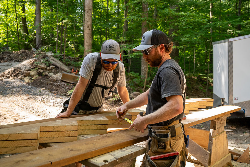 Two men measuring wood planks at an outdoor construction site.