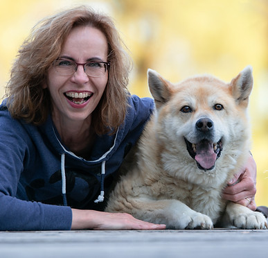 Hundebesitzerin liegt mir ihrem Hund auf dem Boden und lächelt in die Kamera
