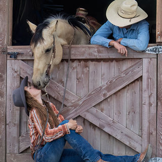 Cowgirl giving a kiss to horse leaning over barn door.