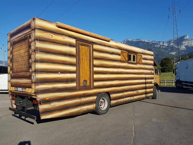 Poids-lourd décoré en trompe-l'œil de rondins de bois façon chalet suisse, avec une carte du monde à l'arrière.