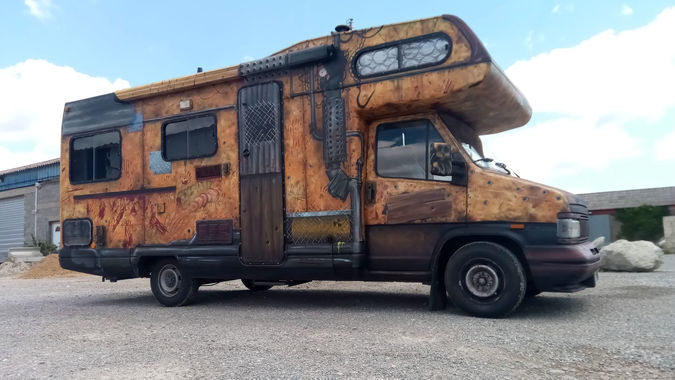 Camping-car personnalisé avec un décor post-apocalyptique, effet rouille, tôle rivetée et impacts de balles façon Mad Max.