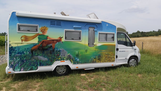 Fresque réaliste du Petit Prince et du renard devant un coucher de soleil sur la carrosserie d'un camping-car.