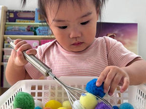 A child plays with colorful pom-poms during sensory play.