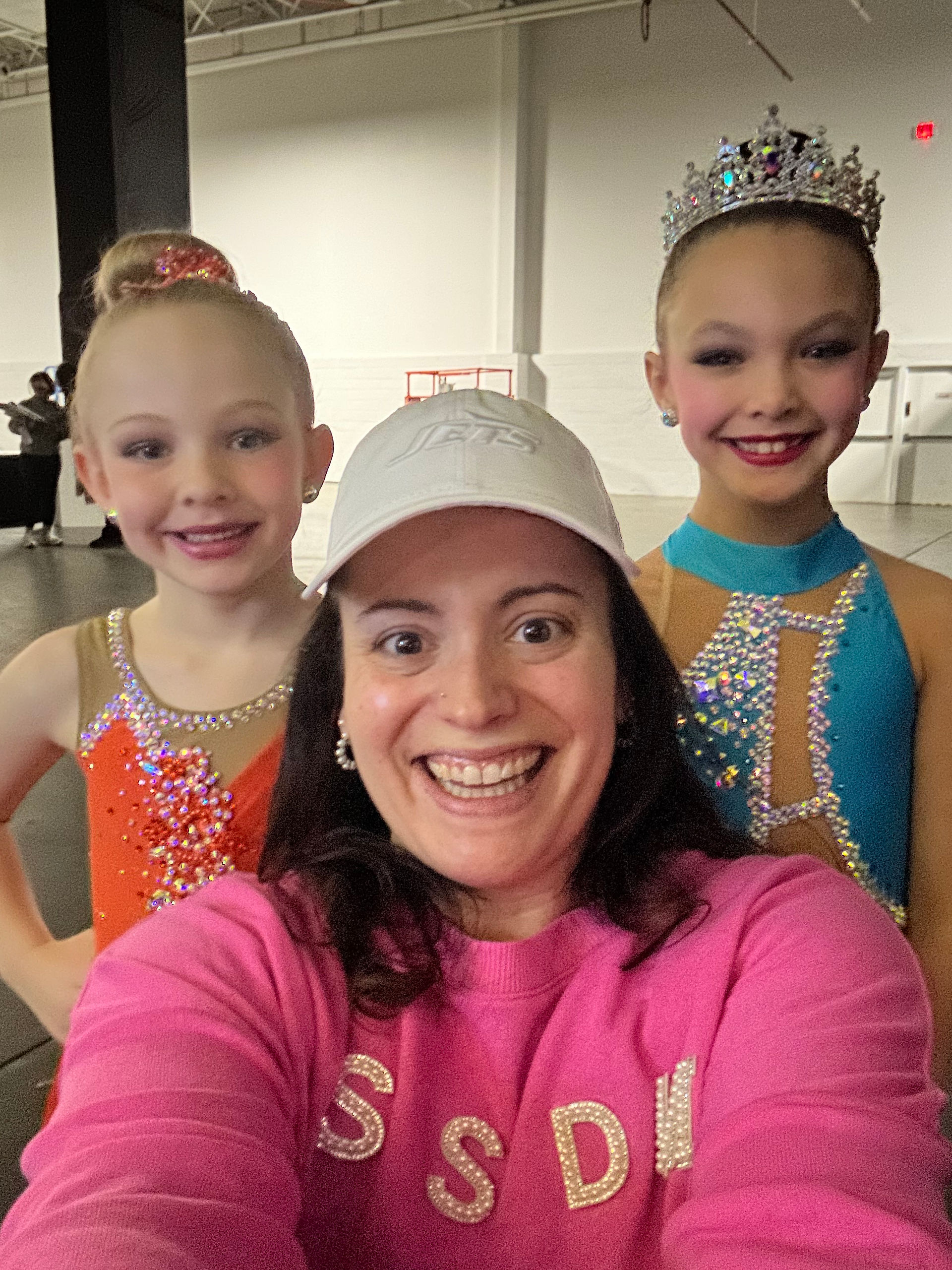 Three smiling girls in dance costumes and a woman wearing a white cap.