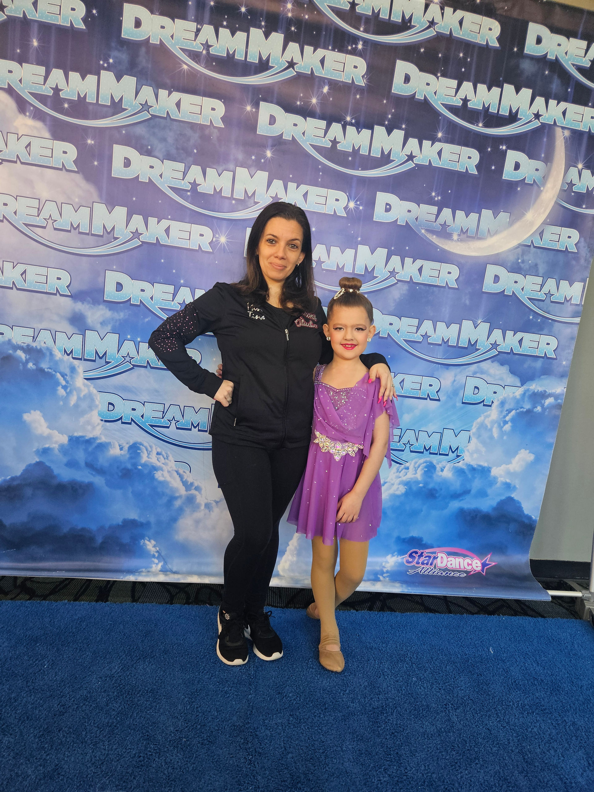 Two females pose in front of a Dream Maker backdrop: DREAM MAKER.