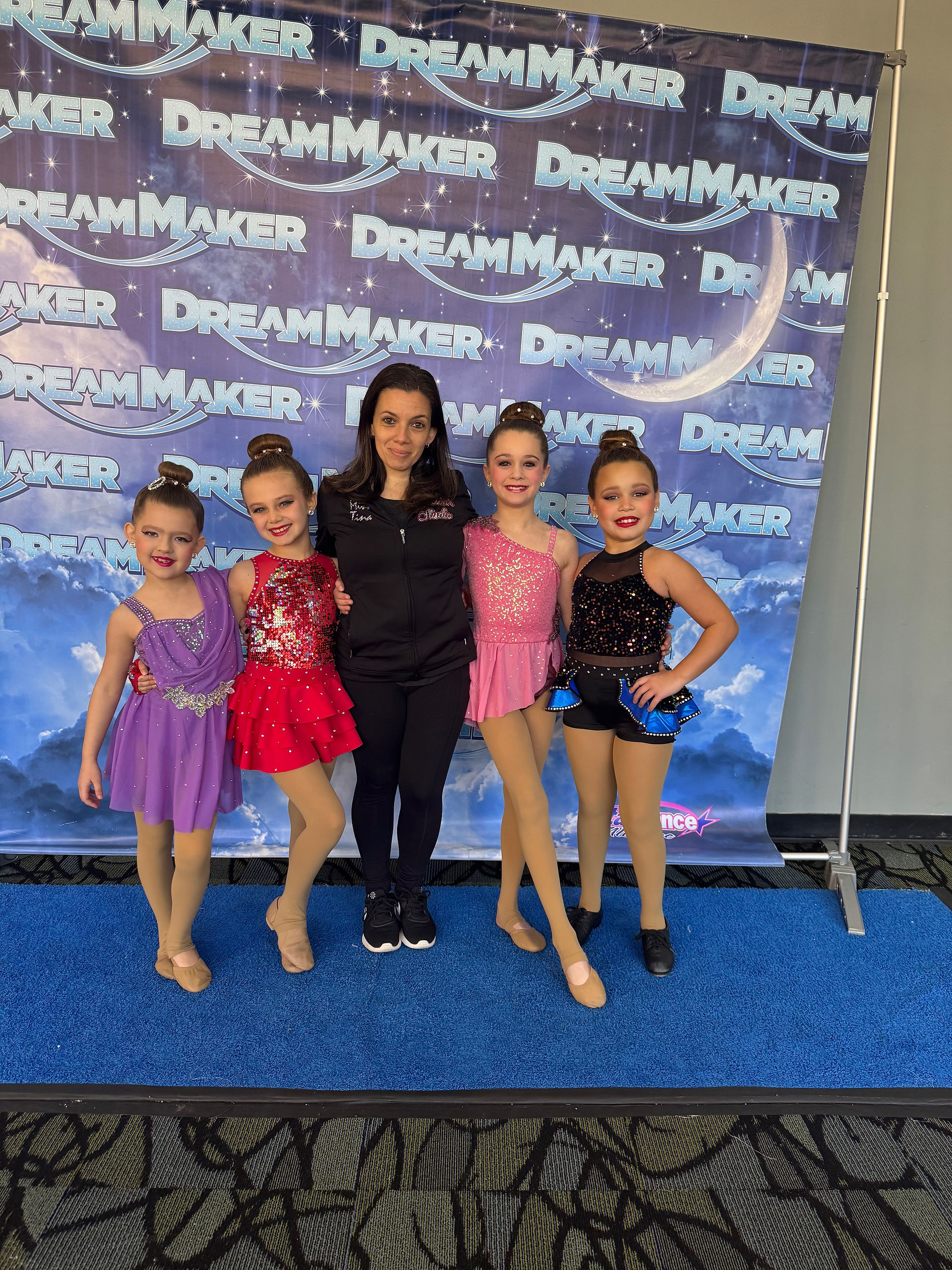 Five young dancers pose with adult against Dream Maker backdrop.