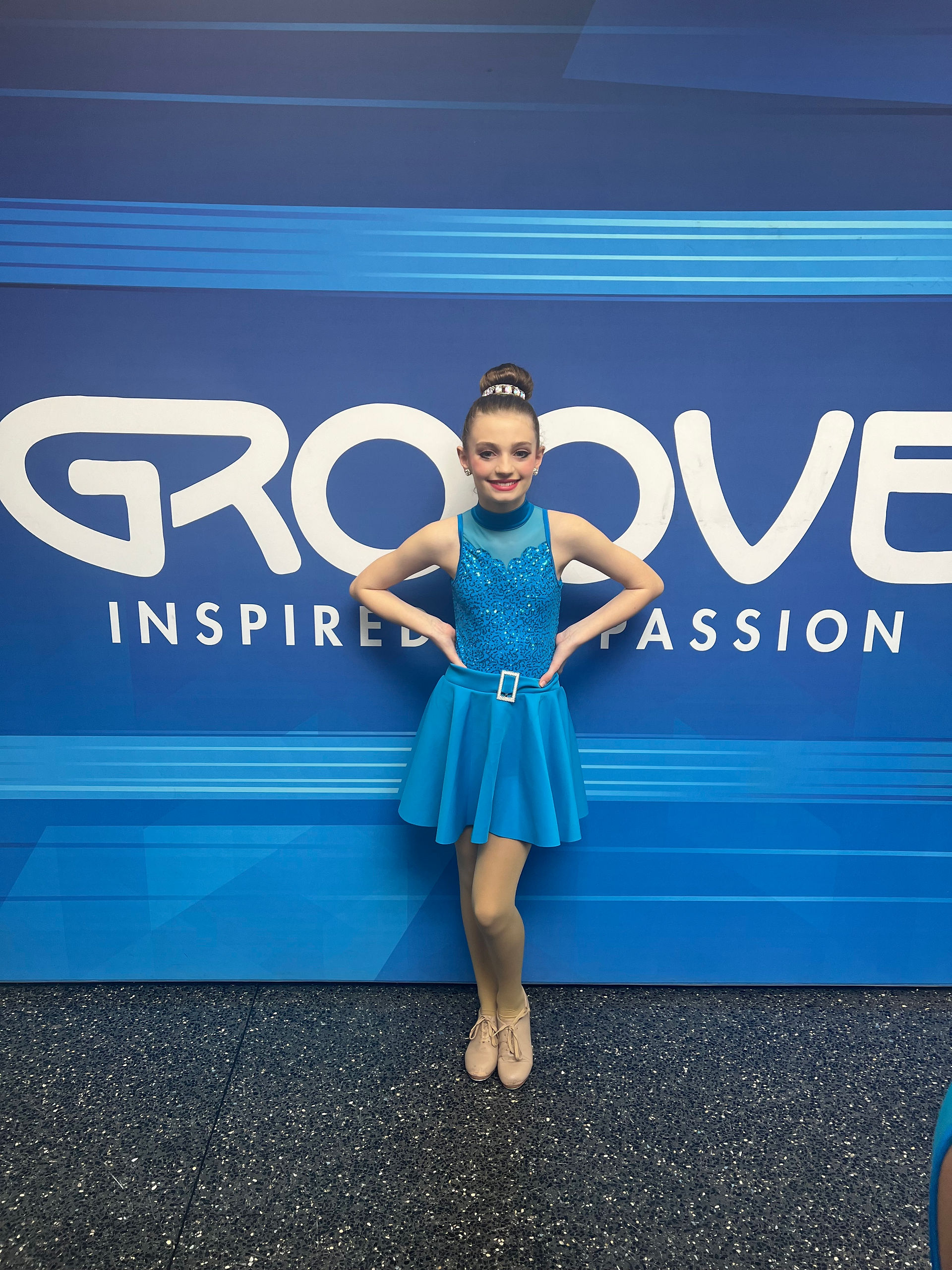 Young dancer in blue outfit against a 'GROOVE' backdrop smiling