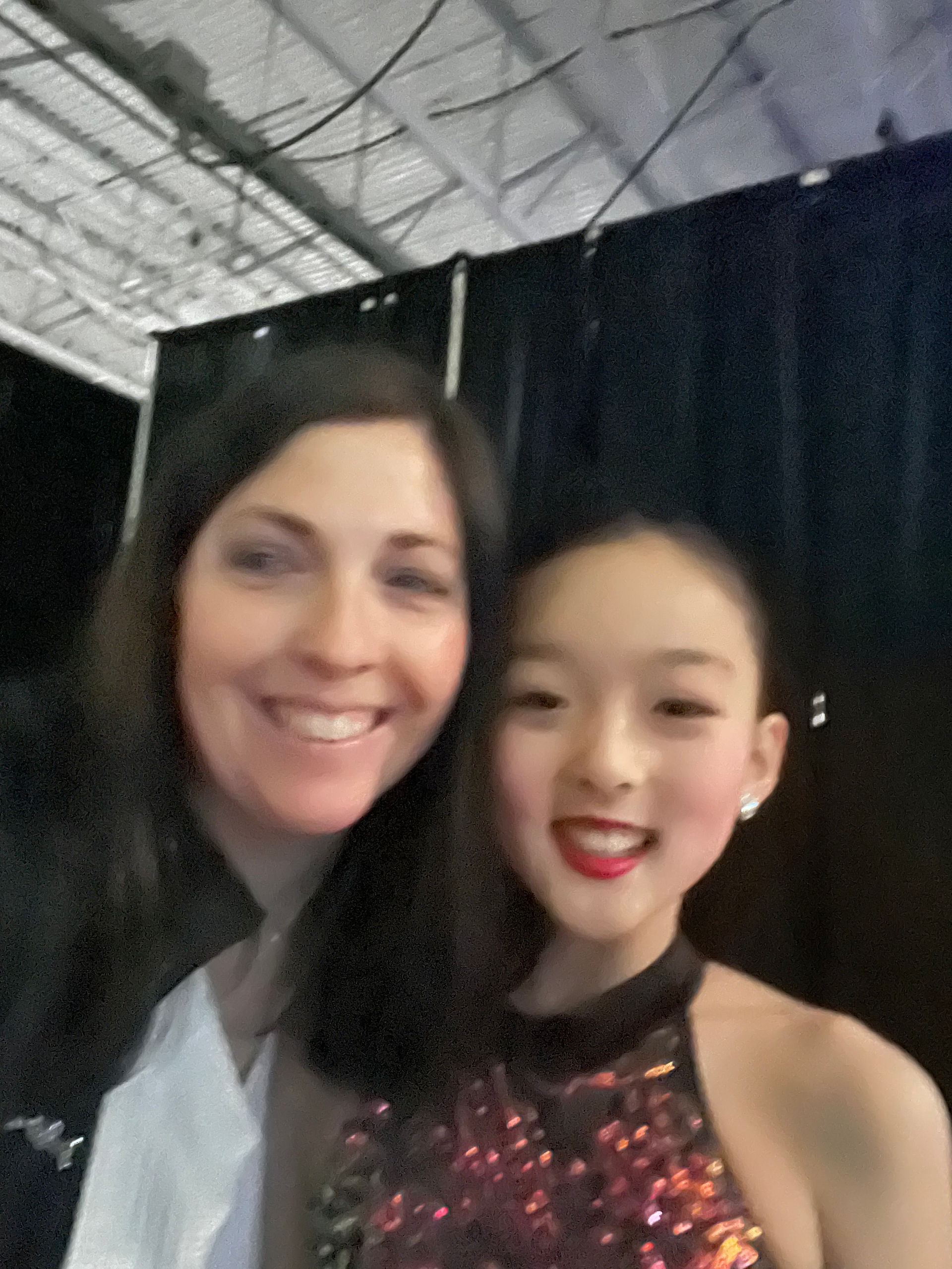 Two smiling women pose for a selfie with a black backdrop.