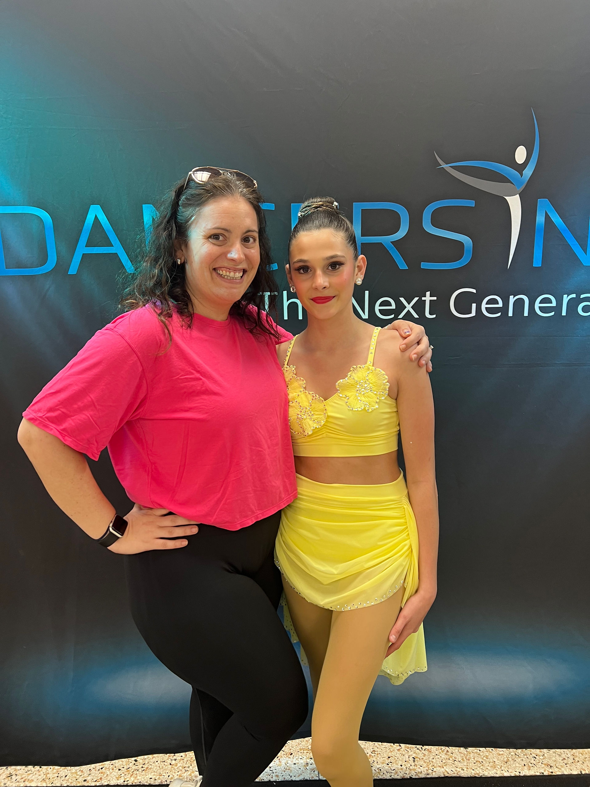 Two women pose in front of a blue Dancer's Inc. sign; The Next Generation.