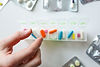 Hand placing a pill into a weekly medication organizer.