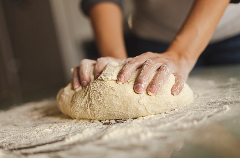 hands kneeding bread dough, on wood surface covered in flour