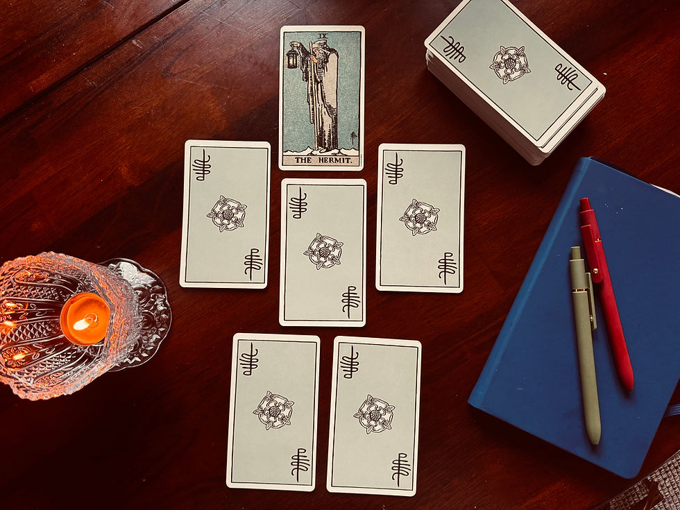 Virgo New Moon tarot spread arranged on a wooden table with the Hermit face-up above five face-down cards, beside a lit candle, tarot deck, journal, and pens.