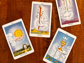 Rider Waite Smith Tarot deck showing ace of wands, ace of swords, ace of cups, ace of pentacles. On wood table background.