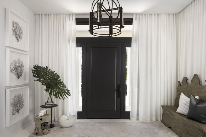 Elegant entryway with black door, white curtains, artwork, and stylish decor.