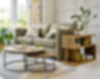 Bright livingroom with nesting tables, a sage green couch, a green and brown striped rug, and matching floral curtains and throw pillows.