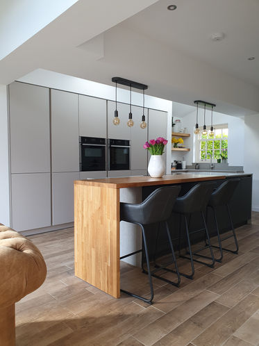 Matthew Kirk Interiors made to order handleless kitchen. Matt finished painted door with veneered oak book shelves.  Solid oak bar top and contrasting concrete quartz worksurfaces. Appliances from Neff and Quooker. Installed in Boston Spa, Wetherby, Leeds.