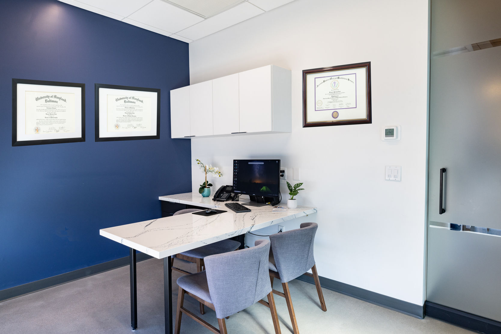 Office with white desk, computer, and framed certificates