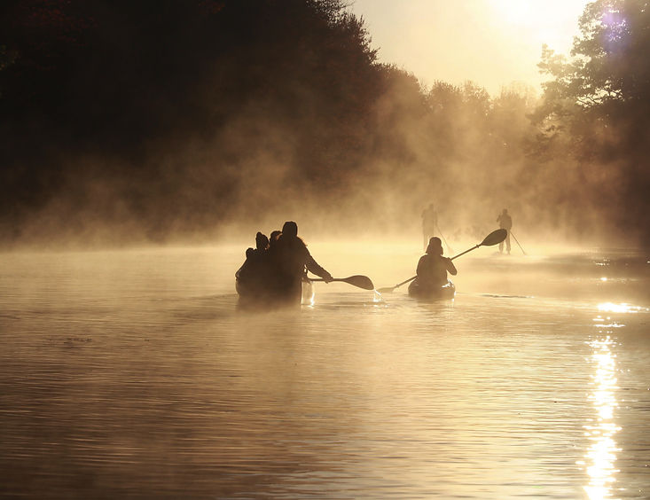 a group canoeing and paddleboarding along a river a sunset