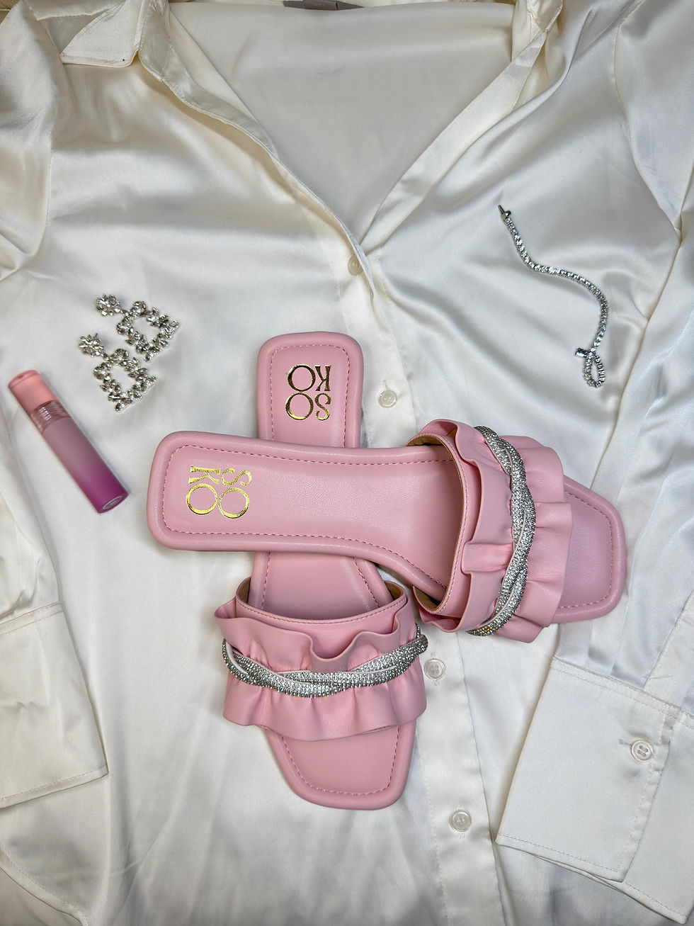 Pink sandals, earrings, lipstick, and silk shirt styled on white surface