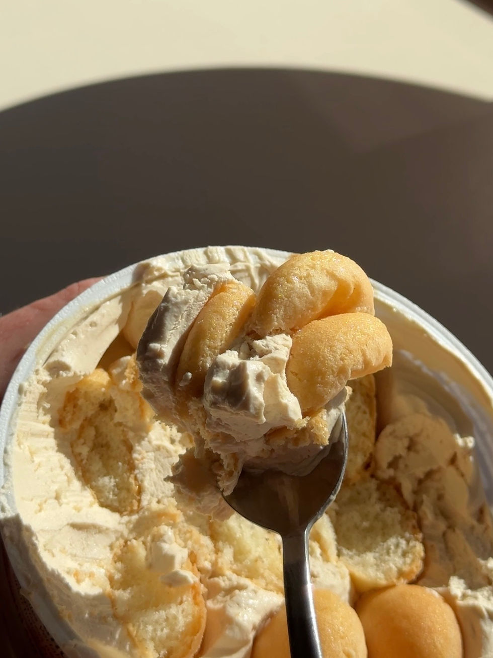 Eine Nahaufnahme eines Dessertbechers mit Löffelbiskuit und Sahne in beige Tönen. Ein Löffel hebt eine Portion heraus.
