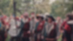 People in medieval costumes with shields and spears, smiling during an outdoor event. Trees in the background, lively atmosphere.