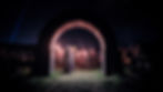 Group in medieval costumes with torches walks through a wooden arch at night, creating a mysterious and historical atmosphere.