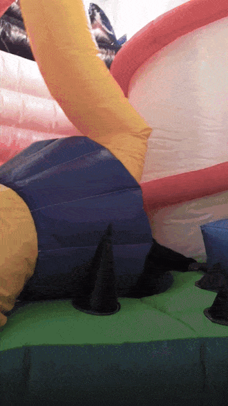 Child playing in a colorful inflatable bounce house with a slide, featuring vibrant red, yellow, and blue sections, creating a lively atmosphere.