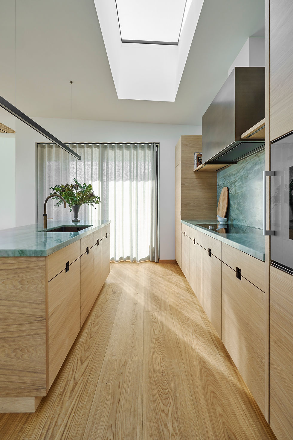 Minimalistisk snedkerkøkken i lys eg med grøn marmorbordplade.