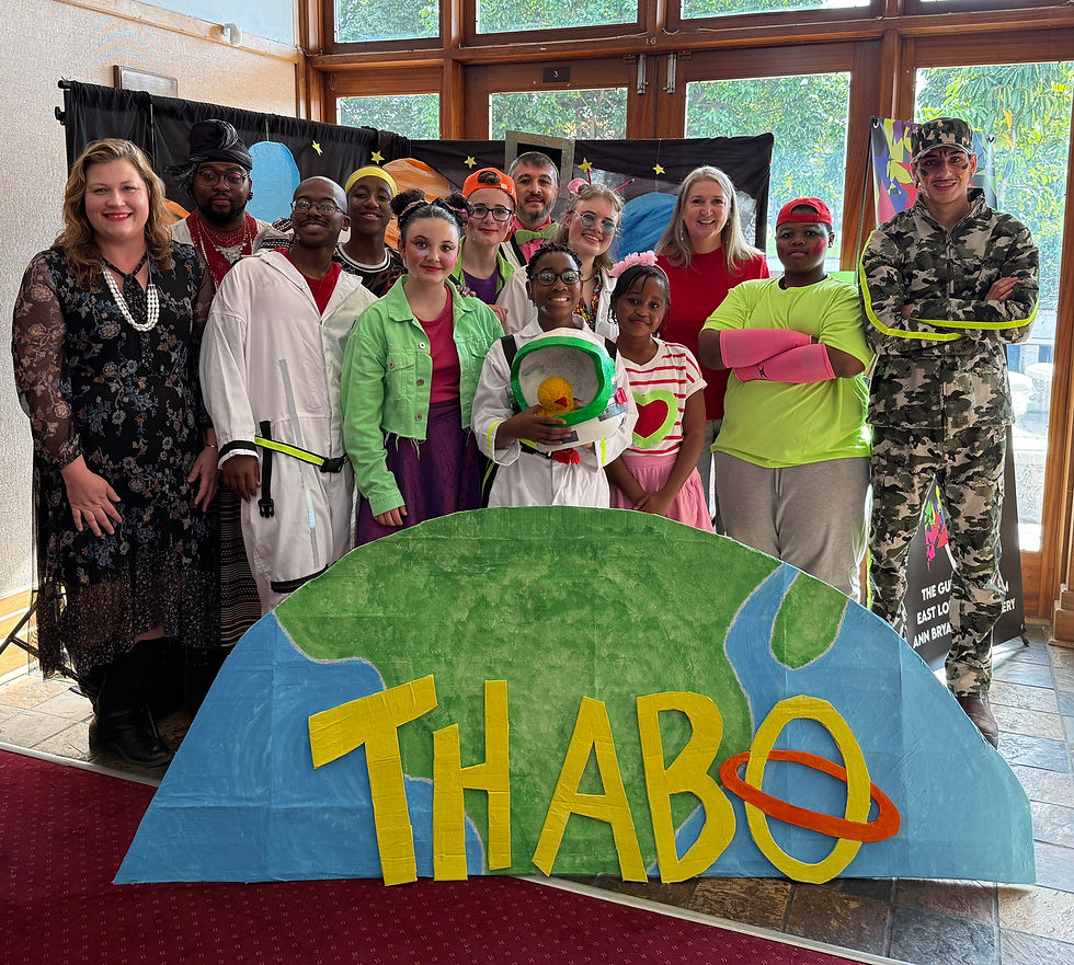 Smiling group in colorful costumes poses indoors before a space-themed backdrop with THABO sign and large Earth cutout.