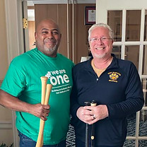 Two men standing and smiling. One is from We Are One Foundation, the second is the donor. Both holding baseball bats that were donated to the foundation.