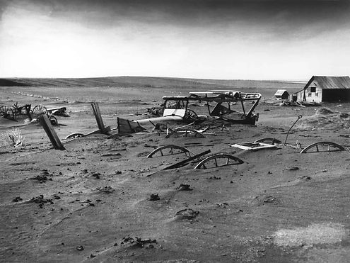 A black and white photo from the “Dust Bowl” showing wagons, cars and buildings buried in sand.