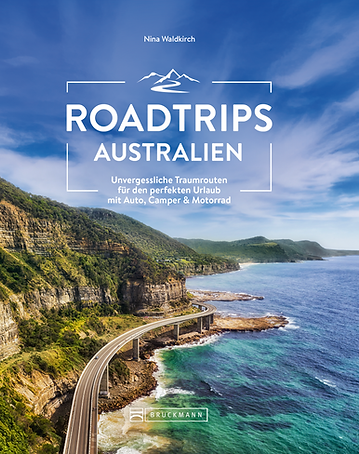 Ein Buchcover, das die Se Cliff Bridge in New South Wales in Australien zeigt. Links neben der Straße liegen grüne Berge, rechts neben der Straße ist das blau-grüne Meer, darüber ein fast wolkenloser blauer Himmel. Der Titel des Buches ist "Roadtrips Australien - Unvergessliche Traumrouten für den perfekten Urlaub mit Auto, Camper & Motorrad", die Autorin "Nina Waldkirch" und der Verlag "Bruckmann".