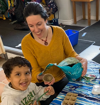 Kindergarten teacher and student smiling and pouring dirt into cups to grow plants