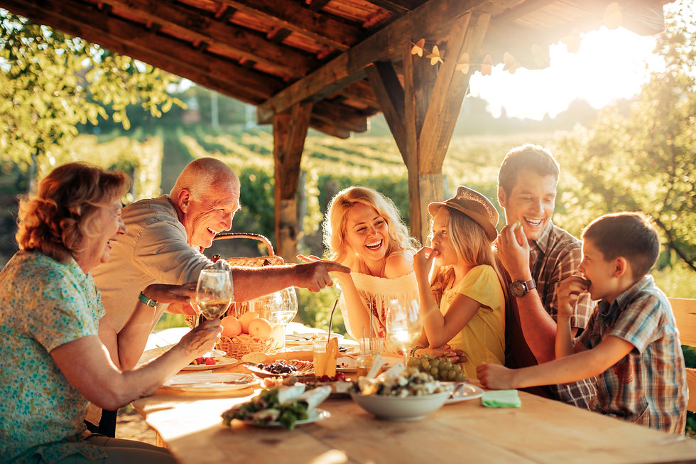 Family enjoys an outdoor meal under wooden pergola. Smiling and laughing, they share fruit and drinks on a sunny day among vineyards.