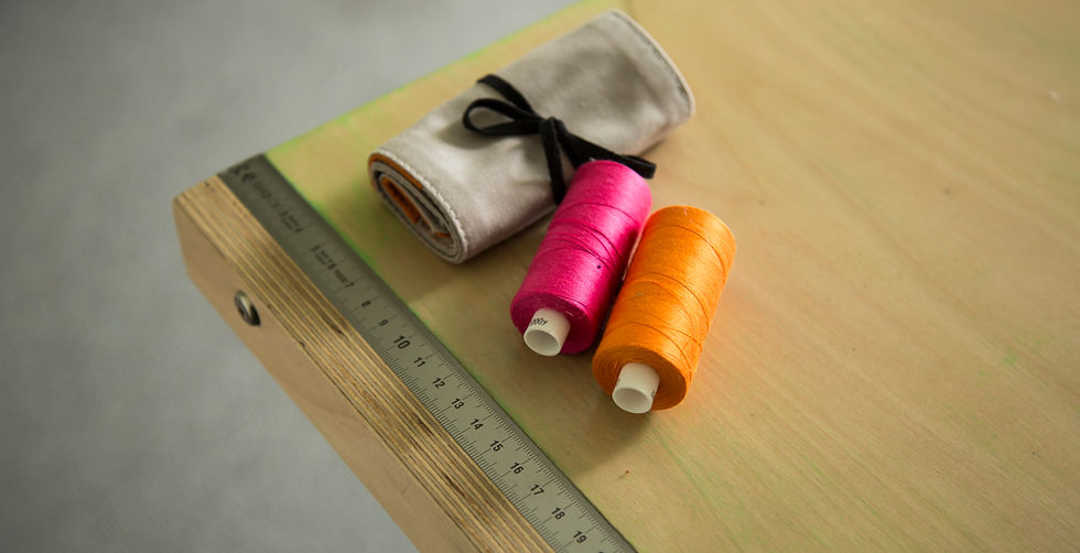 Cutting table and measuring edge in Preloved studio at Canons House. 2 reels of thread - orange & pink and a sewing kit